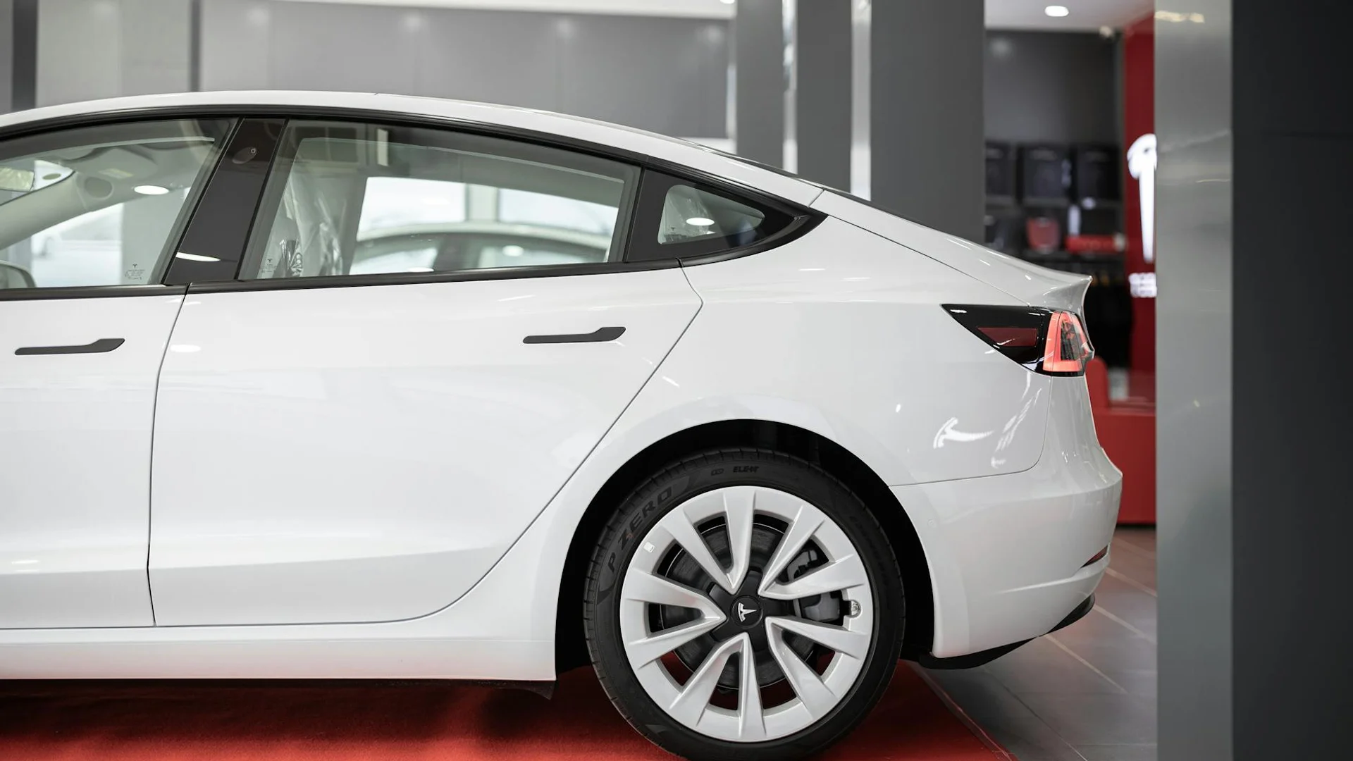 A modern white electric car showcased on a red carpet inside a showroom.