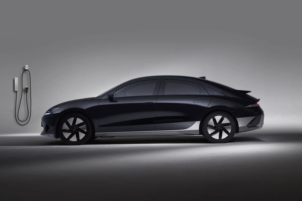 Side view of a black electric car in a studio, showcasing sleek design and charging station.