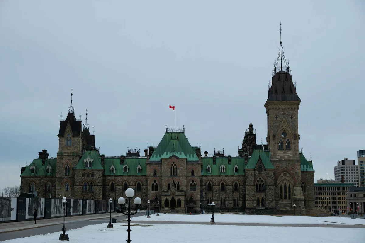 The Parliament of Canada building, with a red Canadian flag flying above its green roof, stands over a snowy ground.