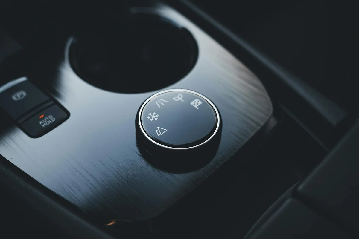 A car's center console with a black rotary dial featuring white icons for driving modes, next to an "AUTO HOLD" button.