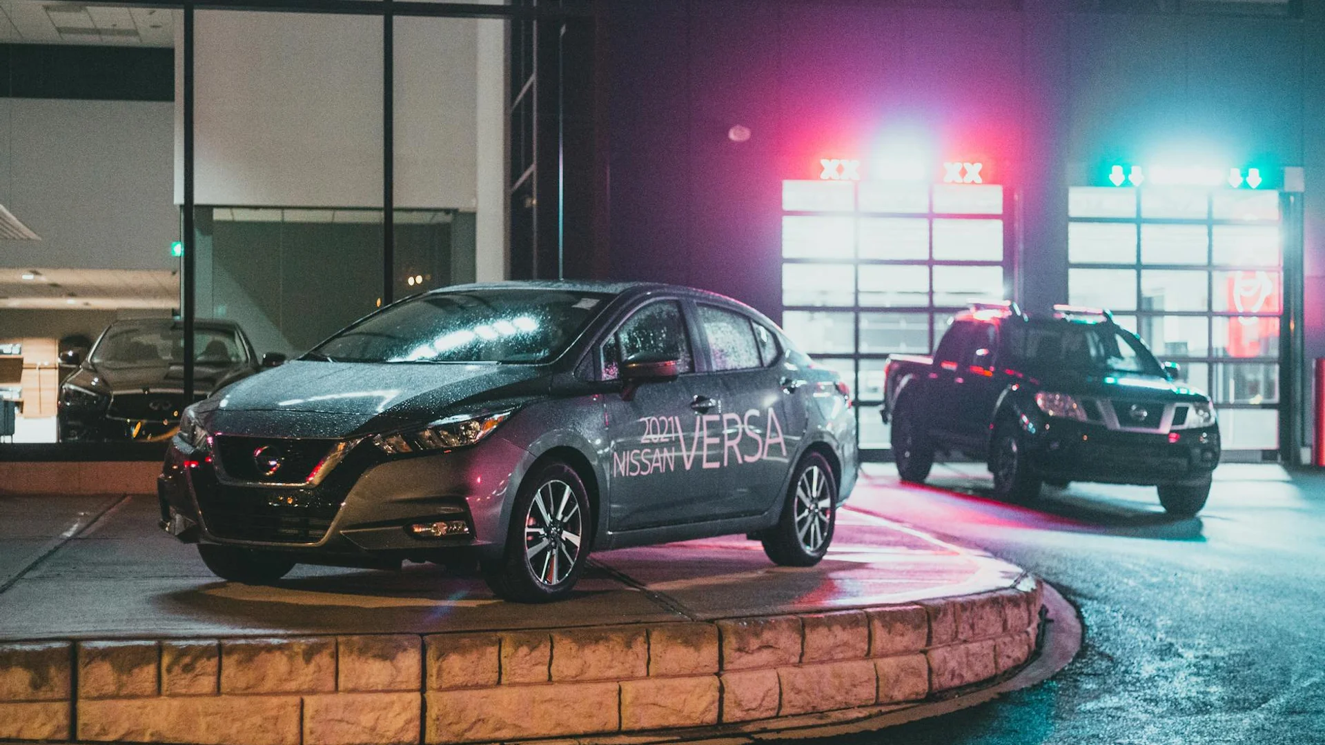 Contemporary dark vehicles placed on pavement in car dealership near glowing glass wall at night