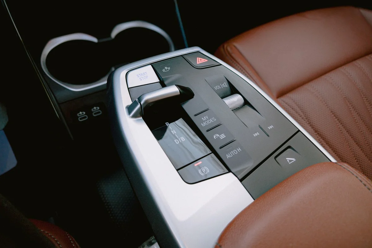 Car center console with a silver gear selector, black control panel, and brown leather seat.