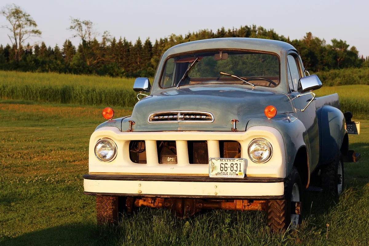 A light blue Studebaker pickup truck with a white grille is parked in a grassy field.
