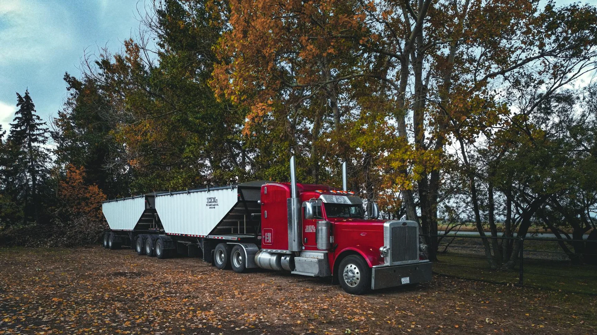 A red trailer truck parked outdoors surrounded by autumn trees in Purple Springs, Canada.