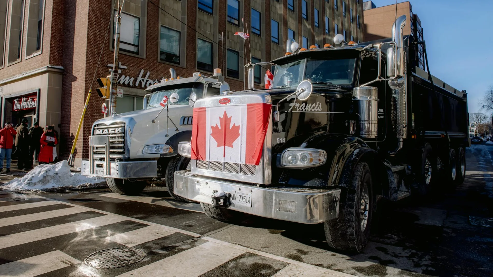 Two trucks with Canadian flags parked on a snowy city street near Tim Hortons in winter.