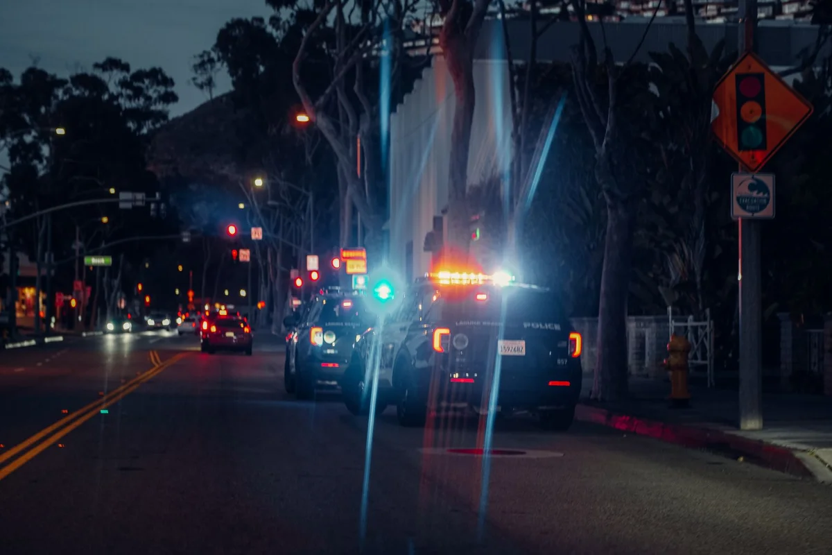 Illuminated police cars parked on a city street at night, creating a dramatic urban scene.
