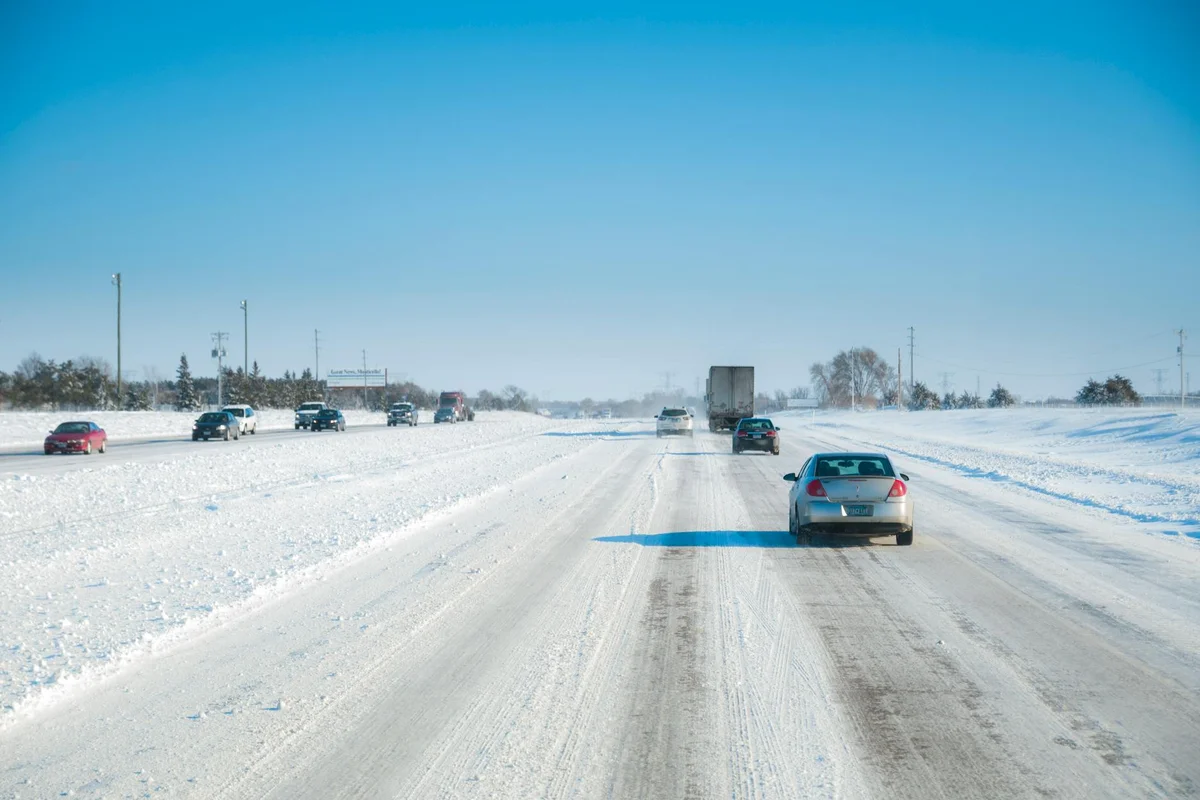 Vehicles travel along a scenic snowy highway under a clear blue sky.