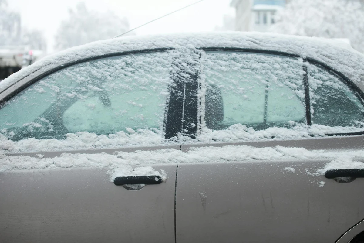 A car covered in snow parked outdoors during winter with frosted windows.