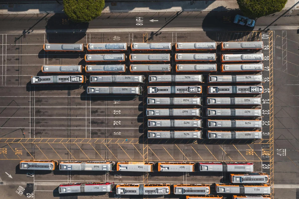 An aerial view shows dozens of orange and gray buses parked in rows on a dark asphalt lot.