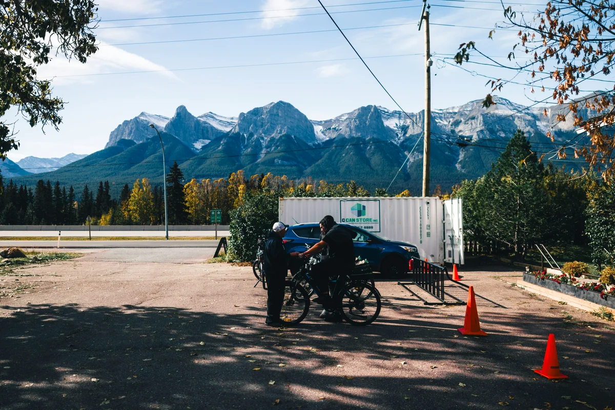 Two people with bicycles near a car and mountains.
