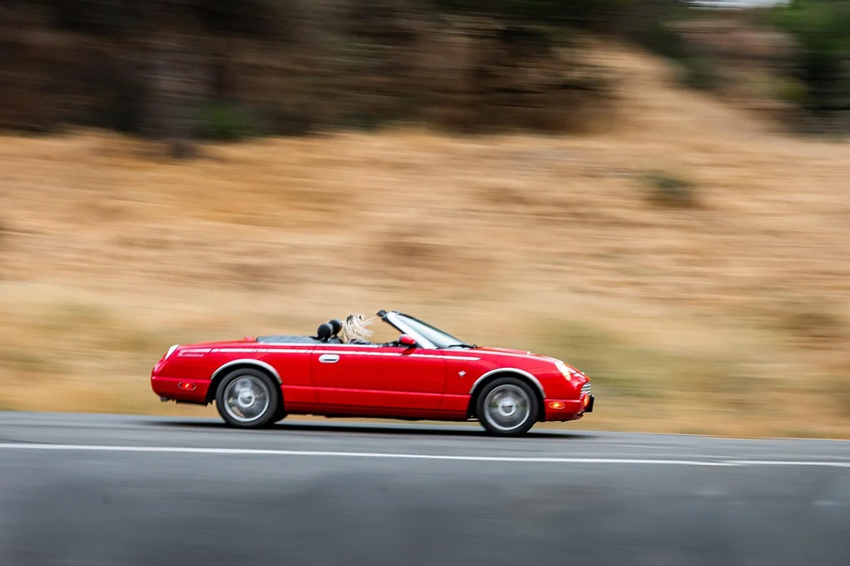 A red convertible drives right on a blurred road with a person's blonde hair visible.