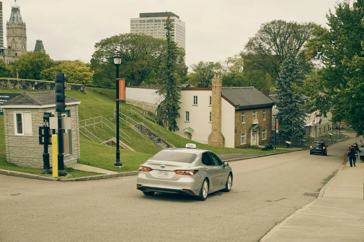 Taxi driving on a quiet street in Quebec City with historic buildings and lush trees.