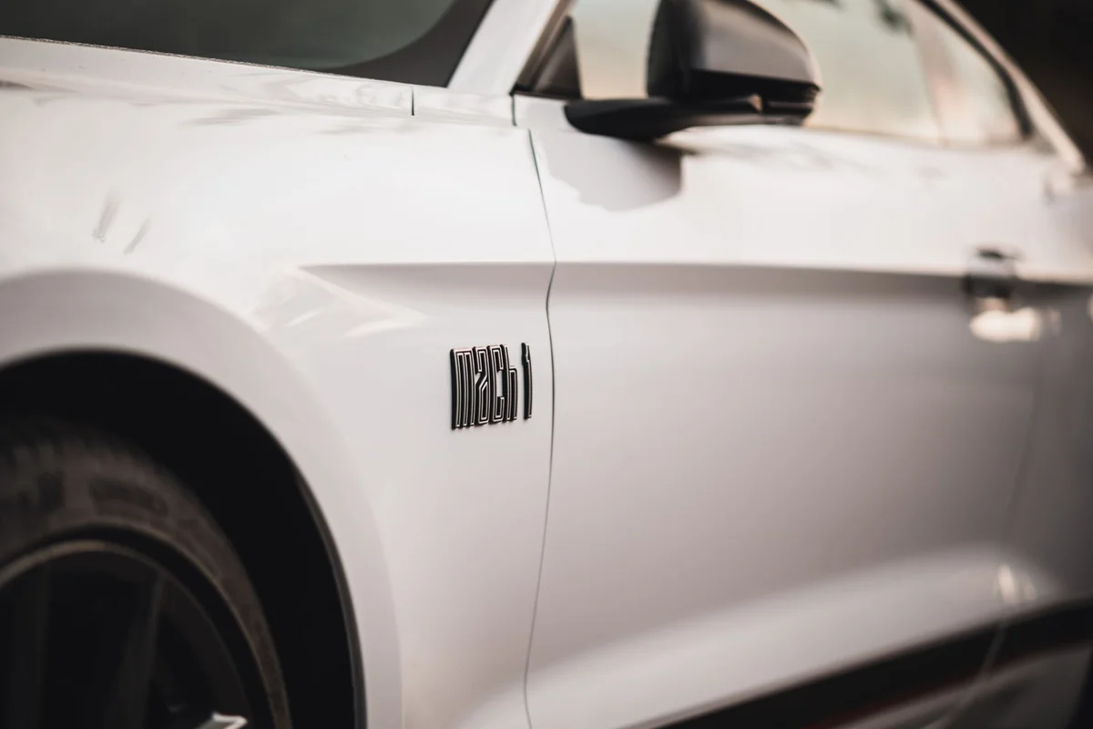 Detailed close-up shot of a sleek white Ford Mustang Mach 1 car door, featuring the Mach 1 badge.