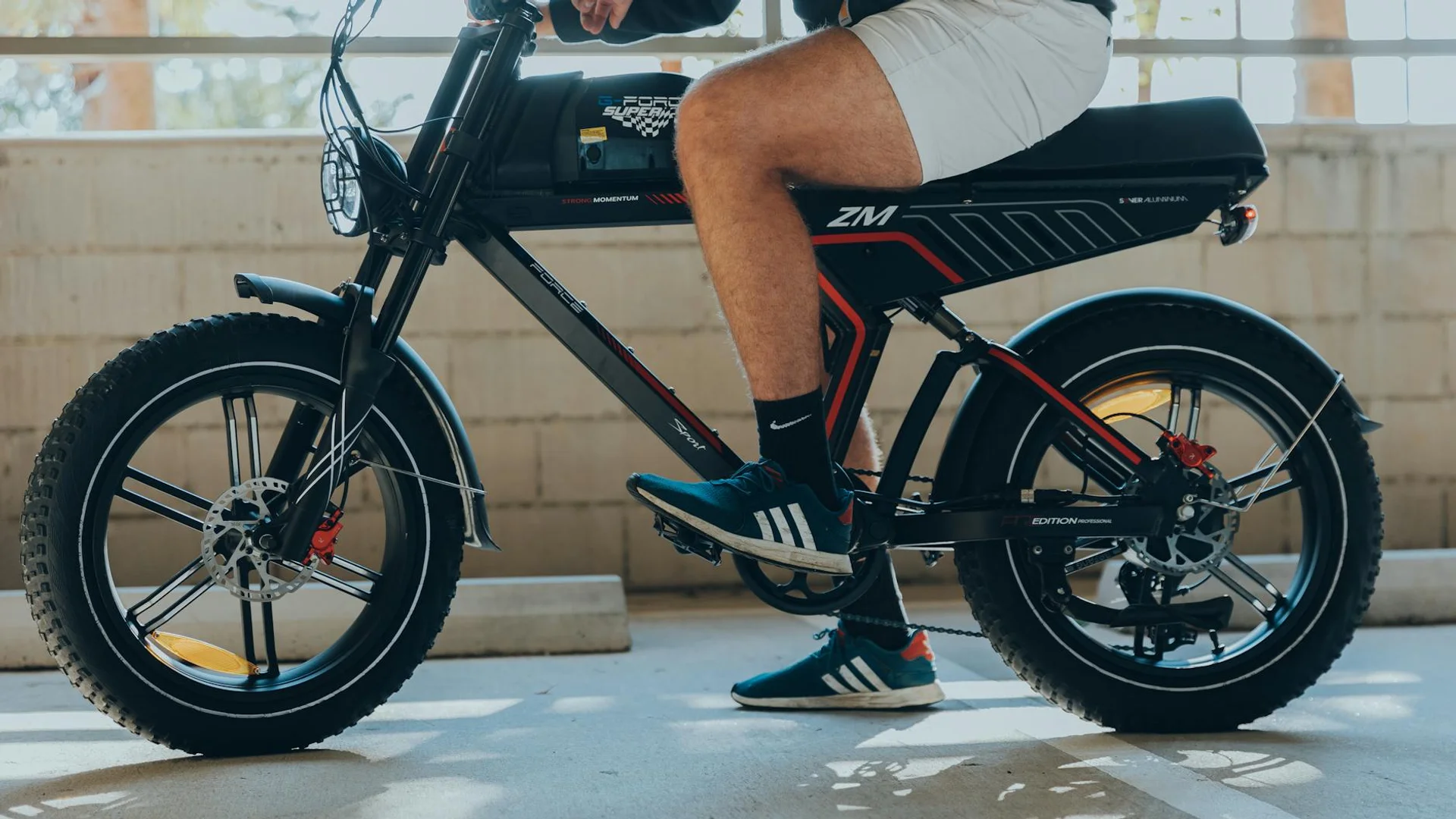 A person with white shorts and blue sneakers sits on a black electric bike with red accents.