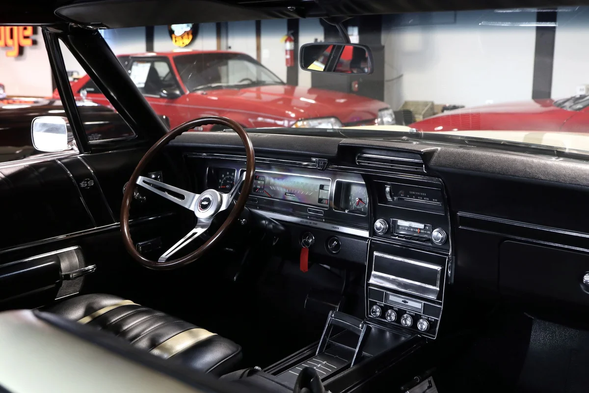 The black interior of a vintage car features a wooden steering wheel and a dashboard with gauges.