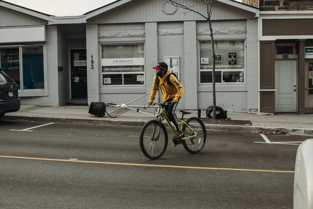 A cyclist in a yellow jacket rides a bike on a Milton street past a community building.