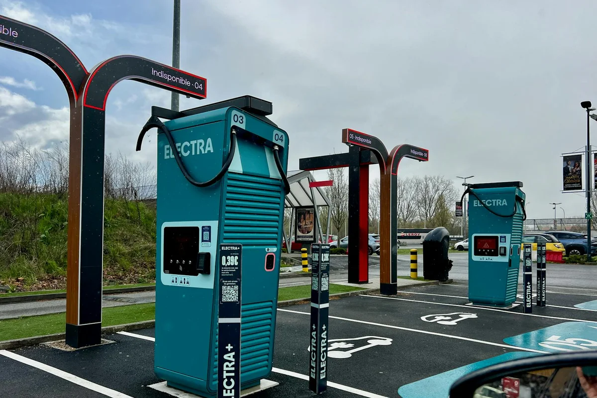A modern electric vehicle charging station in a parking lot on a cloudy day.