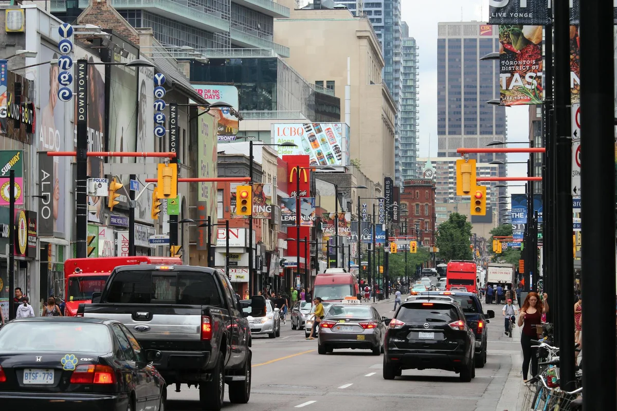 A bustling street scene of Yonge Street in downtown Toronto, filled with vehicles and pedestrians.