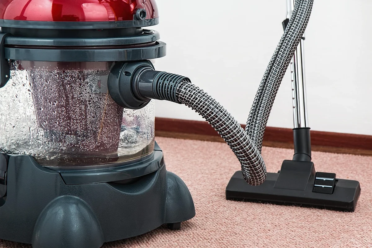 A red and black wet vacuum cleaner with a clear water tank full of bubbles sits on a pink carpet.