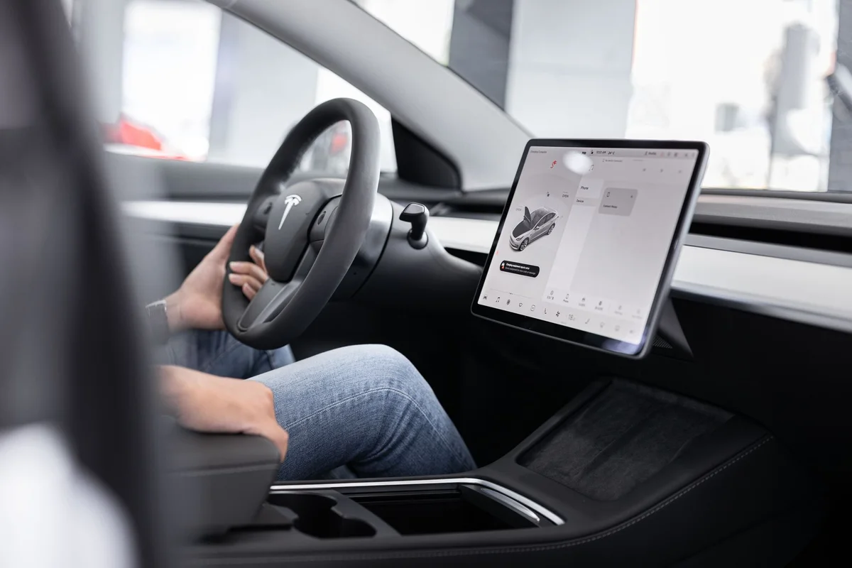 Interior of an electric car showing steering wheel and large touchscreen display, indicating modern technology.