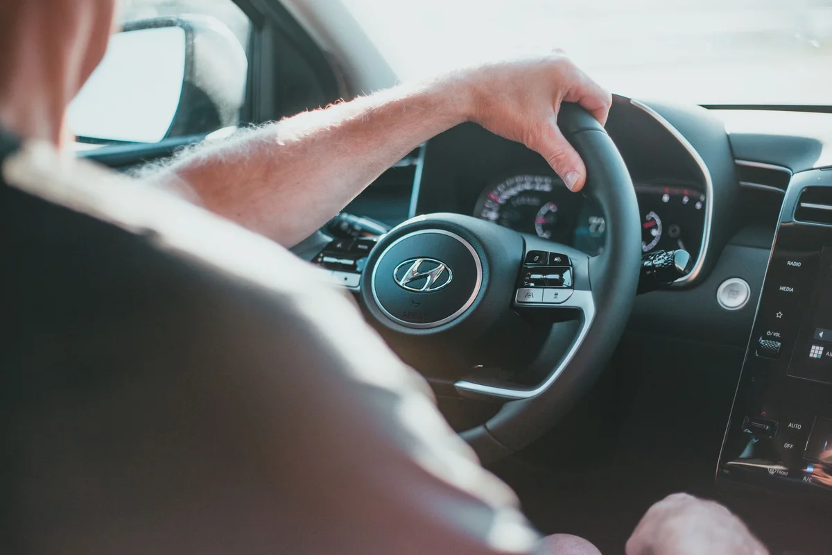 A person's arm and hand grip a black steering wheel with a silver Hyundai logo.