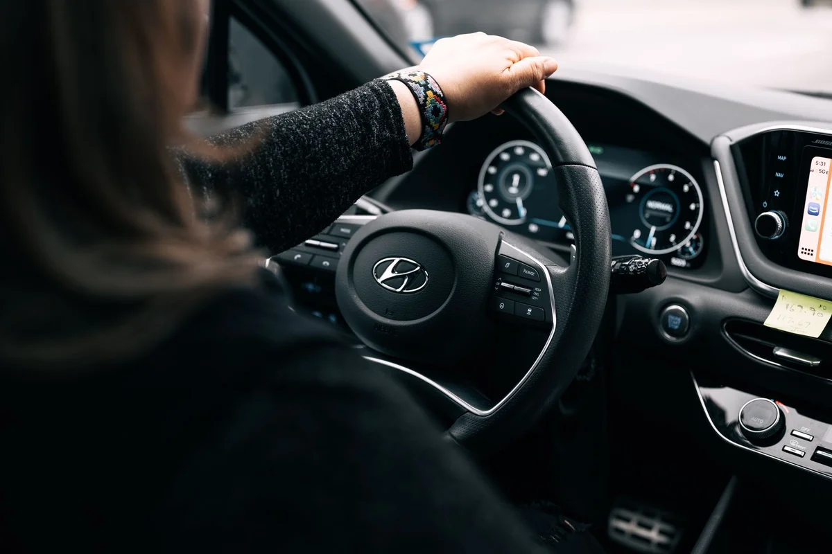 A person with a colorful bracelet on their right wrist holds a black Hyundai steering wheel.