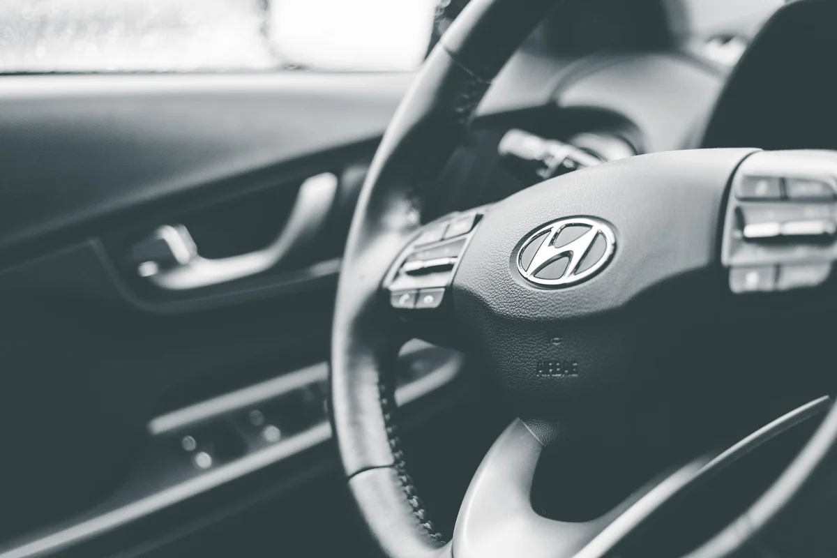 A black and white close-up of a car's steering wheel with a Hyundai logo and control buttons.
