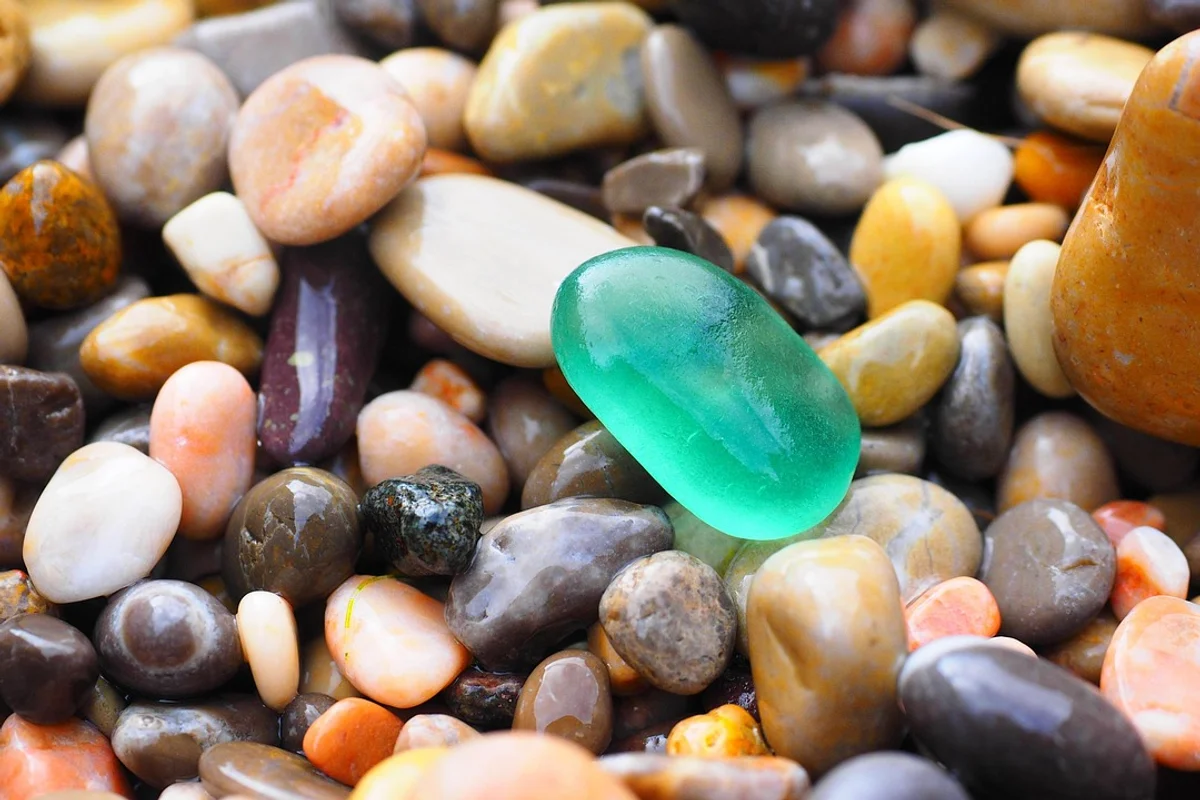 A bright green, smooth, wet pebble rests among many other wet, colorful, and smooth pebbles.