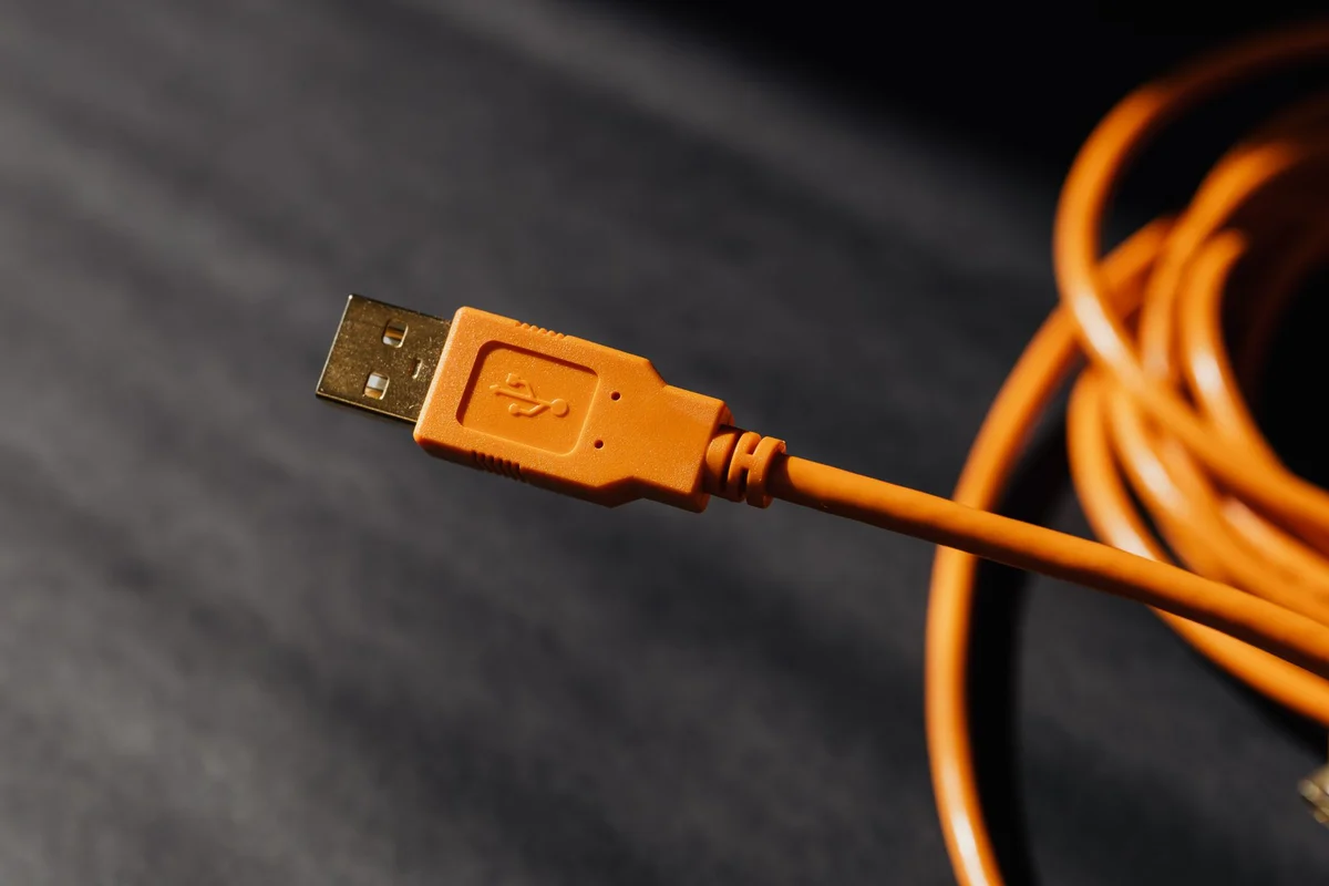 An orange USB-A connector with a gold-colored tip and a coiled cable on a dark background.