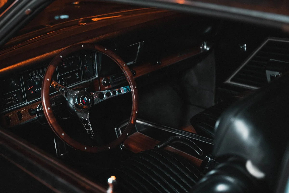 Explore the elegant interior of a classic car featuring a wooden steering wheel and detailed dashboard.