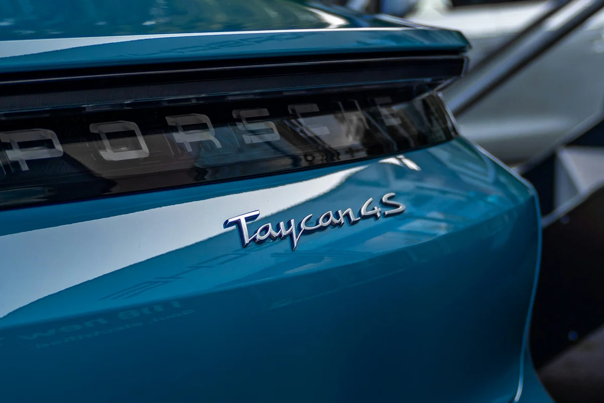 The rear of a teal Porsche Taycan 4S, with the model name in silver script on the trunk.