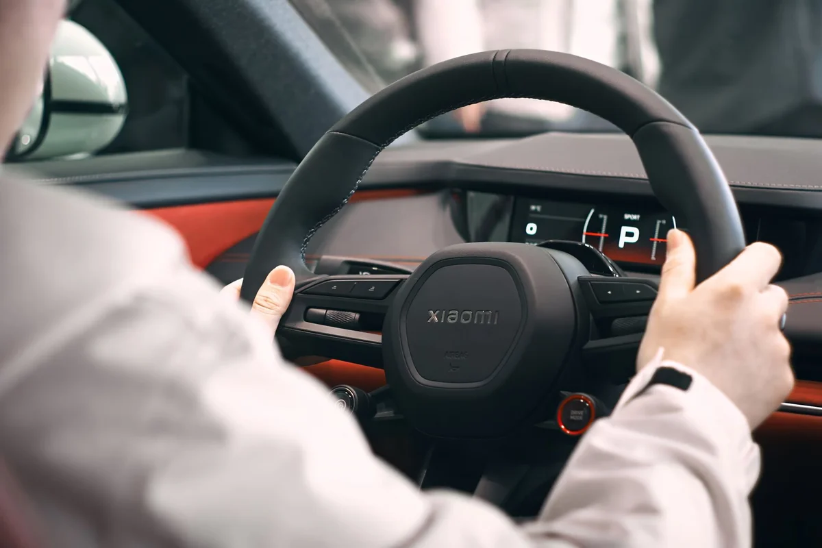 Close-up view of a person holding a steering wheel inside an electric car, focusing on the dashboard.
