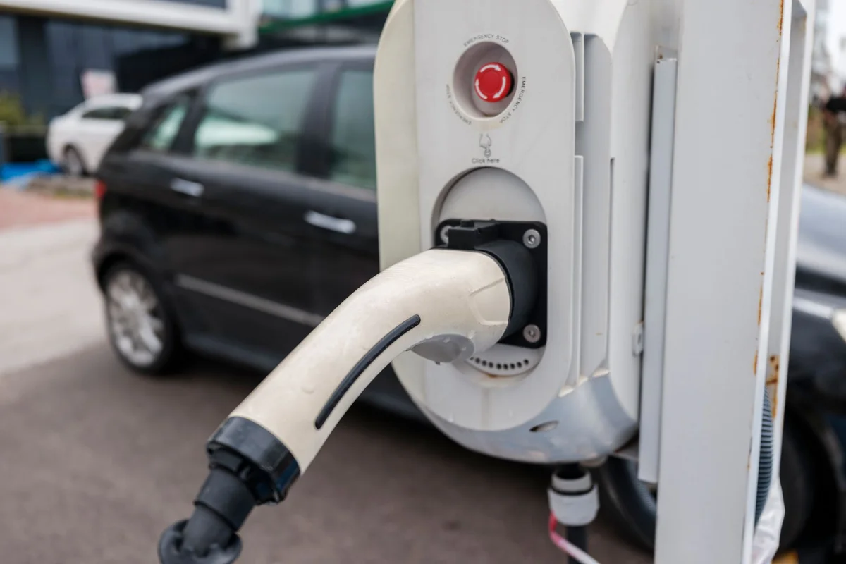 Close-up view of an electric car charging station with a plugged-in charger and cars in an urban environment.