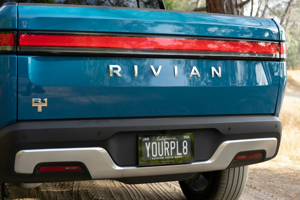 The rear of a teal Rivian truck with a red taillight bar and a "YOURPL8" license plate.