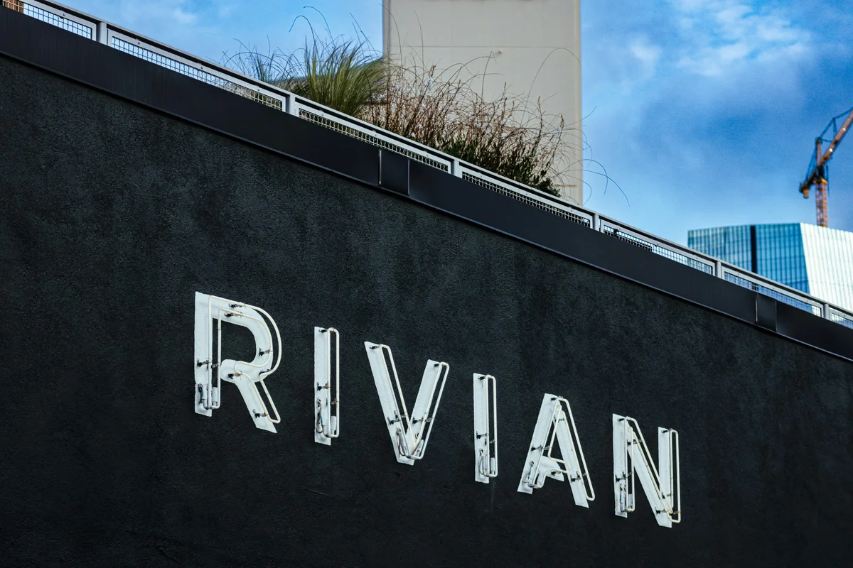 The word "RIVIAN" in white neon letters is mounted on a dark textured wall, with a rooftop garden above.