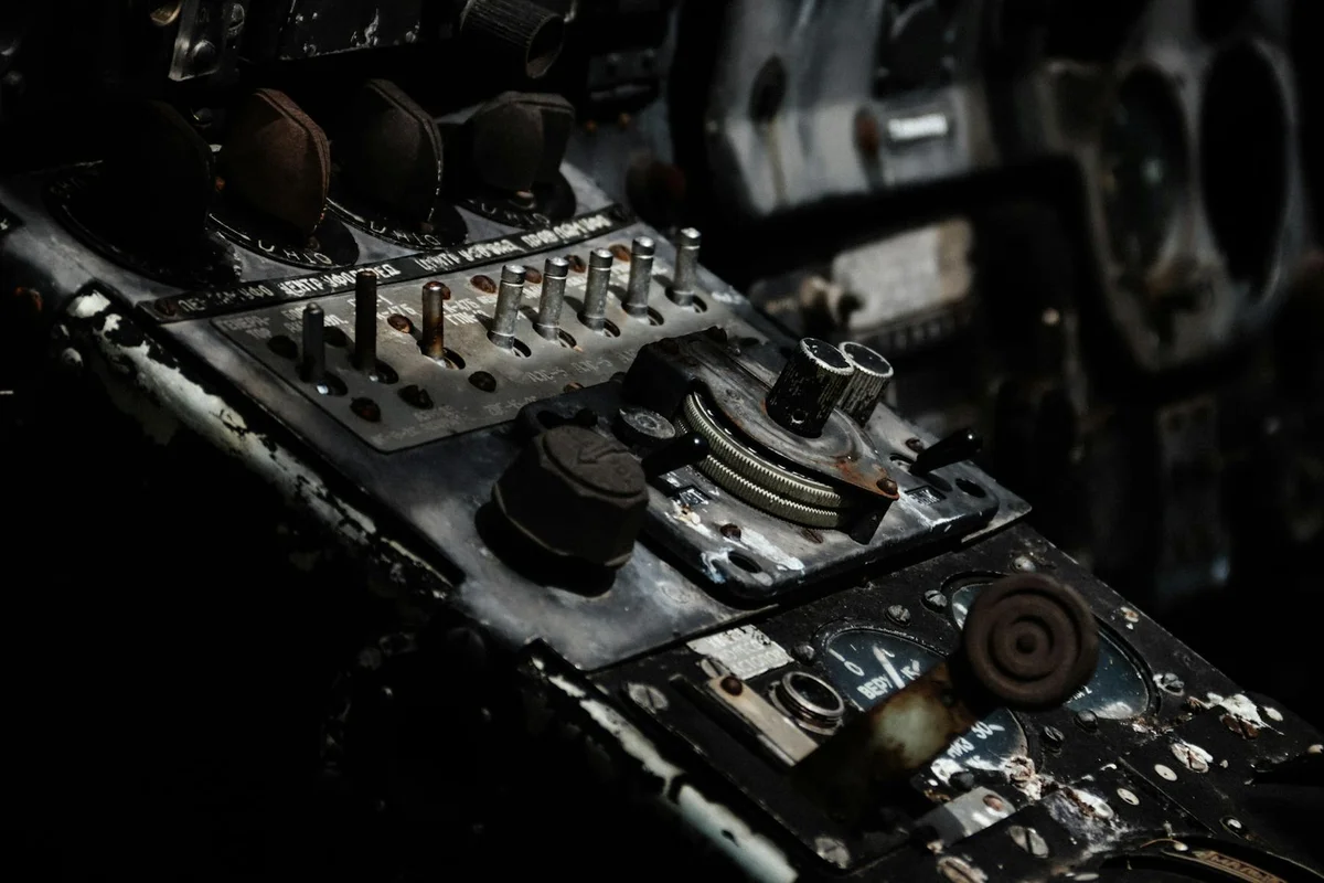 A dark, close-up view of a worn, metallic control panel with numerous switches, dials, and gauges.