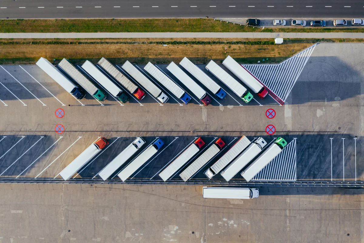 An aerial view of two rows of semi-trucks parked diagonally in a large asphalt lot.