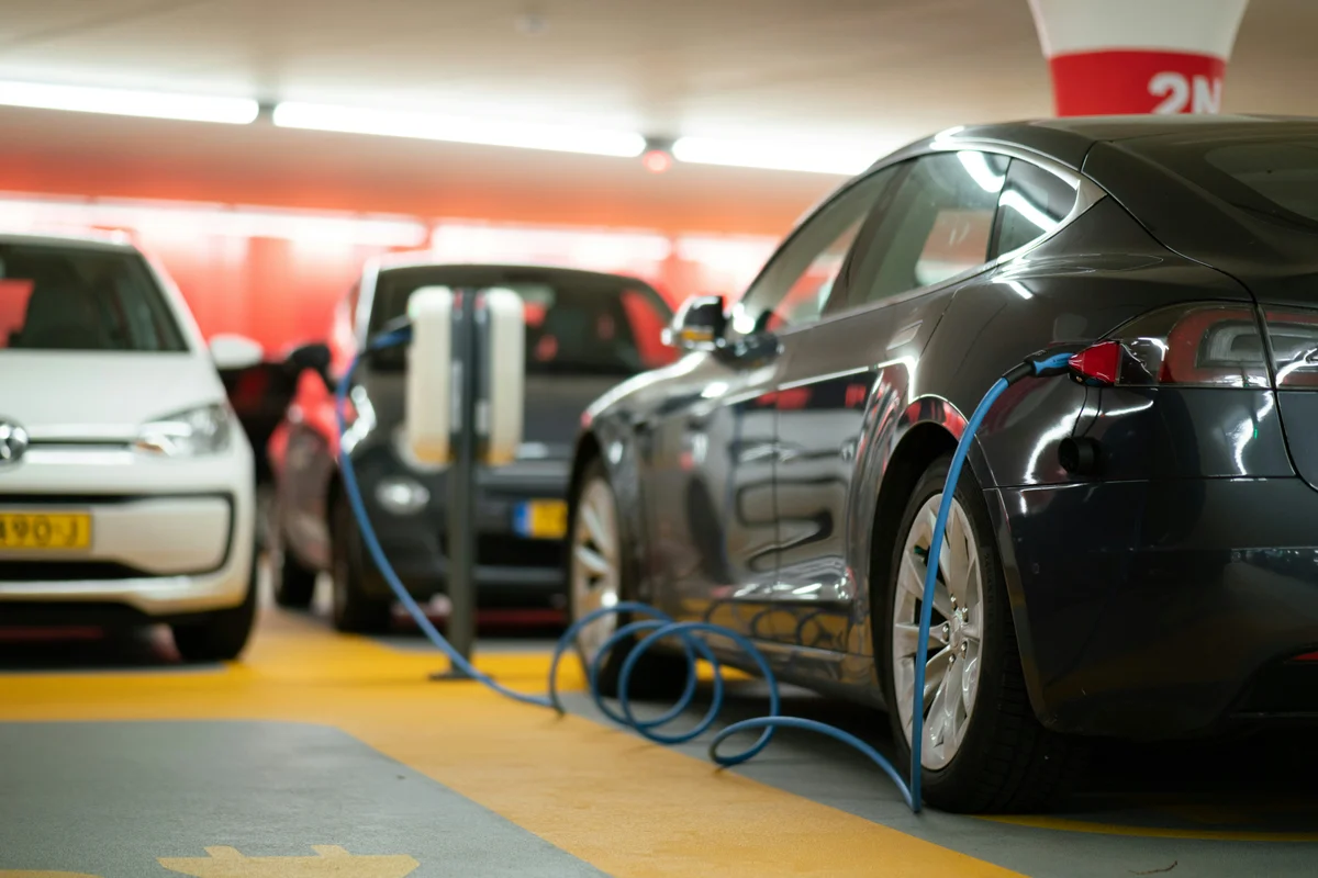 A dark gray electric car is charging with a blue cable in a parking garage.