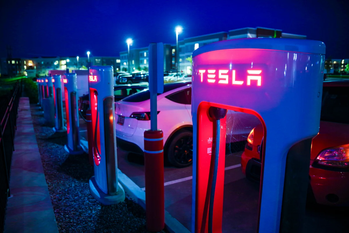 A row of Tesla charging stations with red glowing interiors and a white Tesla car parked at night.