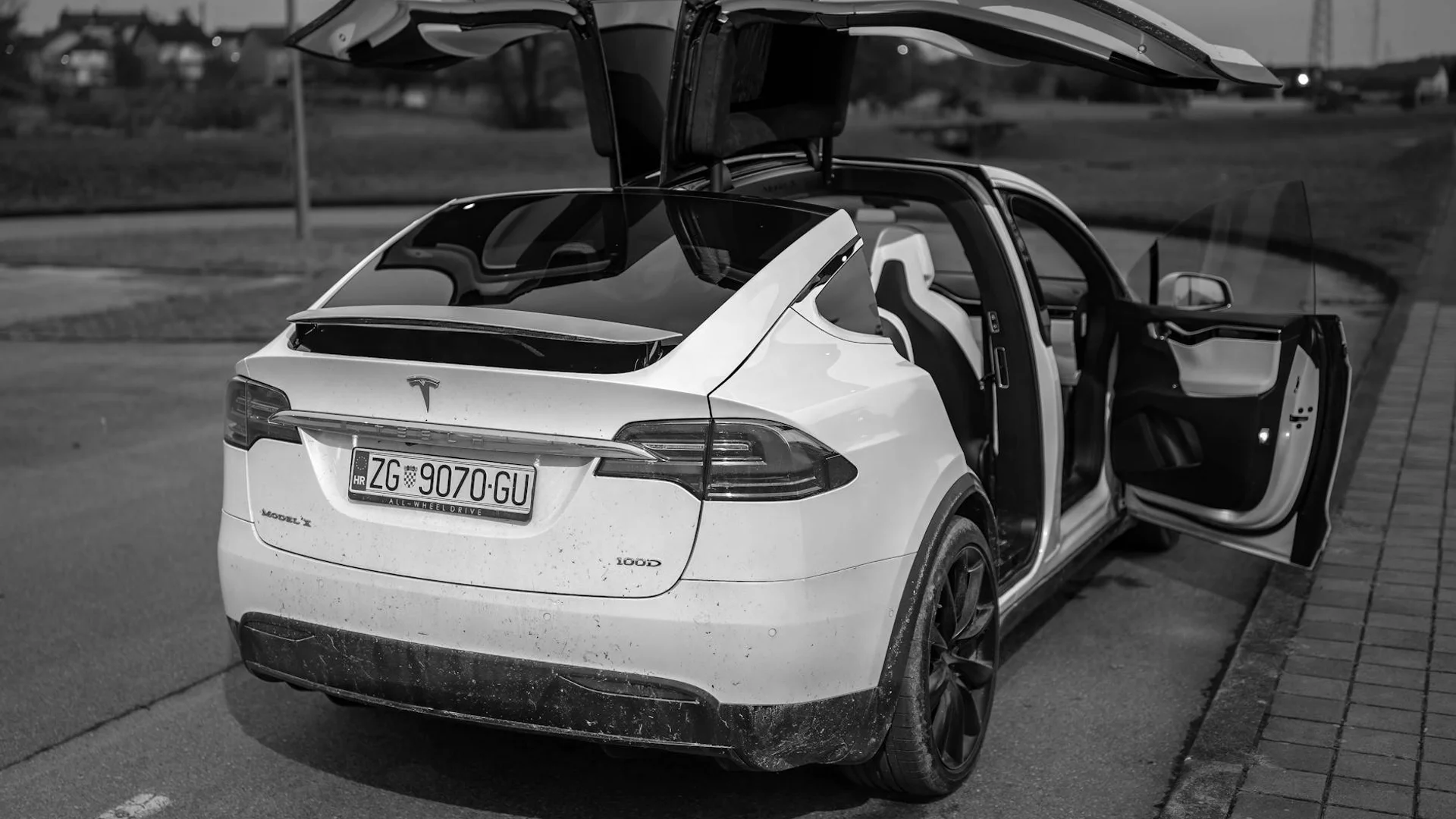 A black and white image of a white Tesla Model X with its falcon wing doors open.