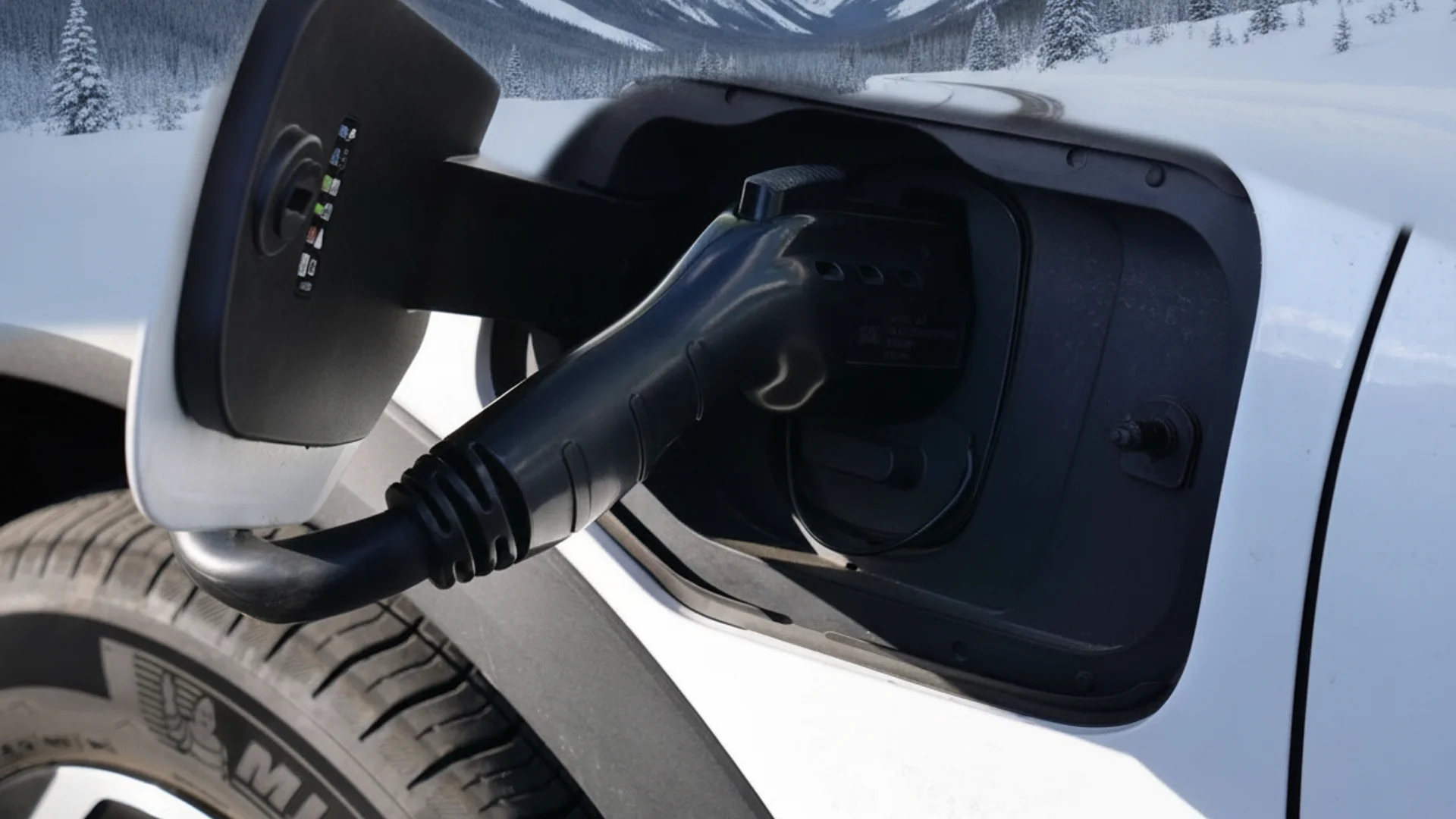 A black EV charging cable is plugged into the white car's port, with a snowy mountain landscape in the background.