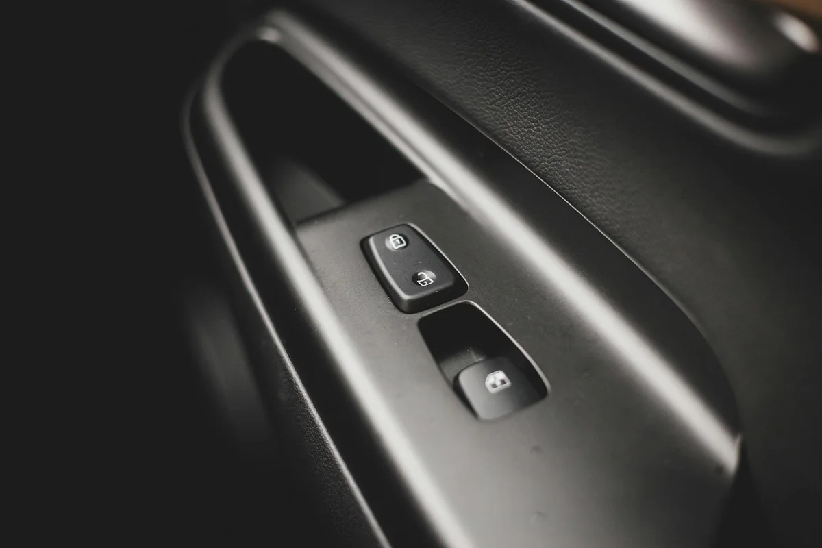 Monochromatic close-up of a car door handle and button panel in soft lighting.