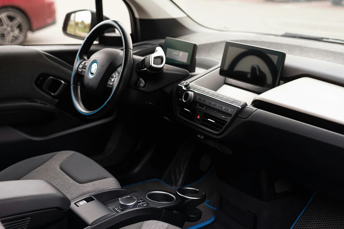 The interior of a car shows a black steering wheel with a blue trim, a dashboard, and a gray seat.