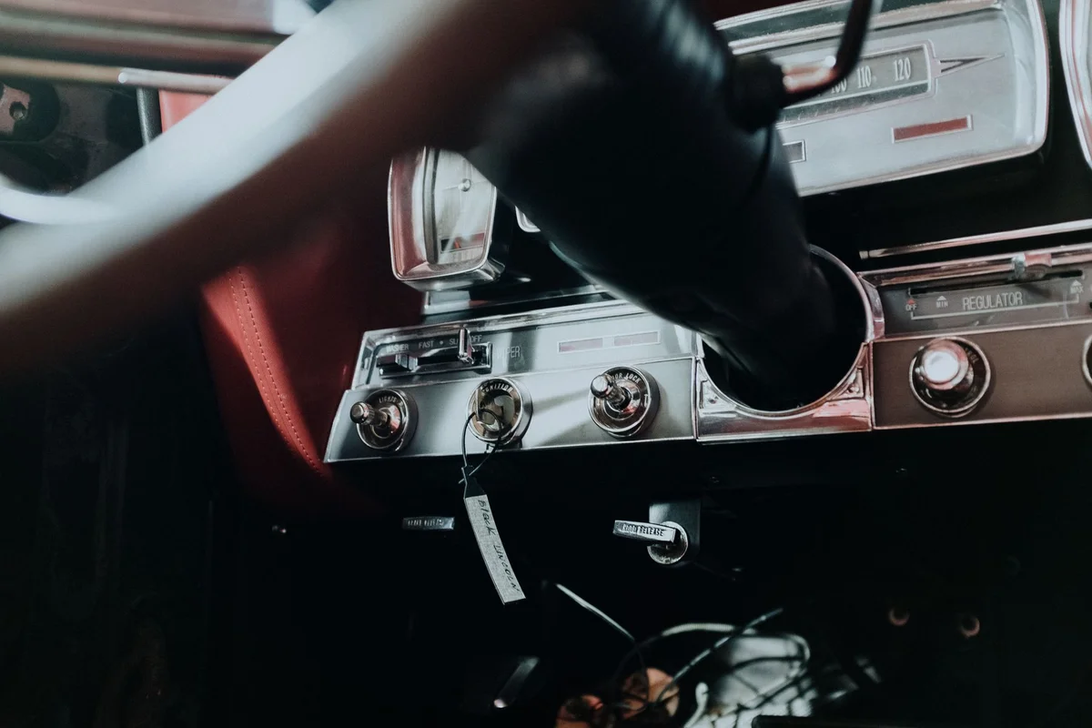 Interior of a vintage car with a beige steering wheel on the right and a black door panel on the left.