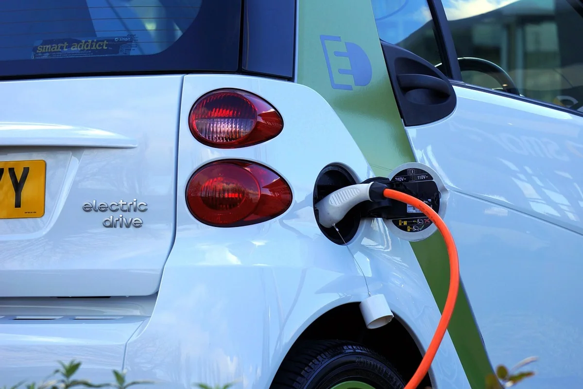 A white electric car is charging, with an orange cable plugged into its side and "electric drive" on the back.