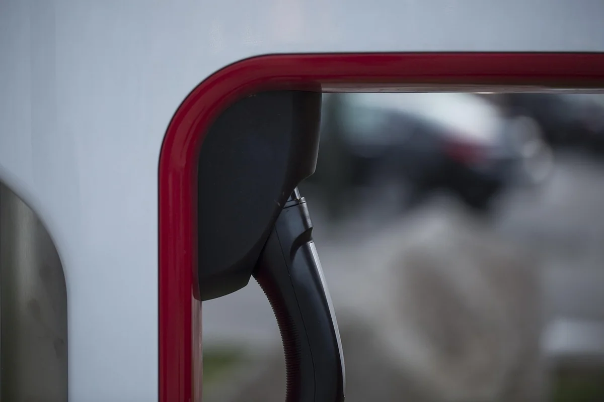 A black electric vehicle charging plug is stored in a white and red charging station.