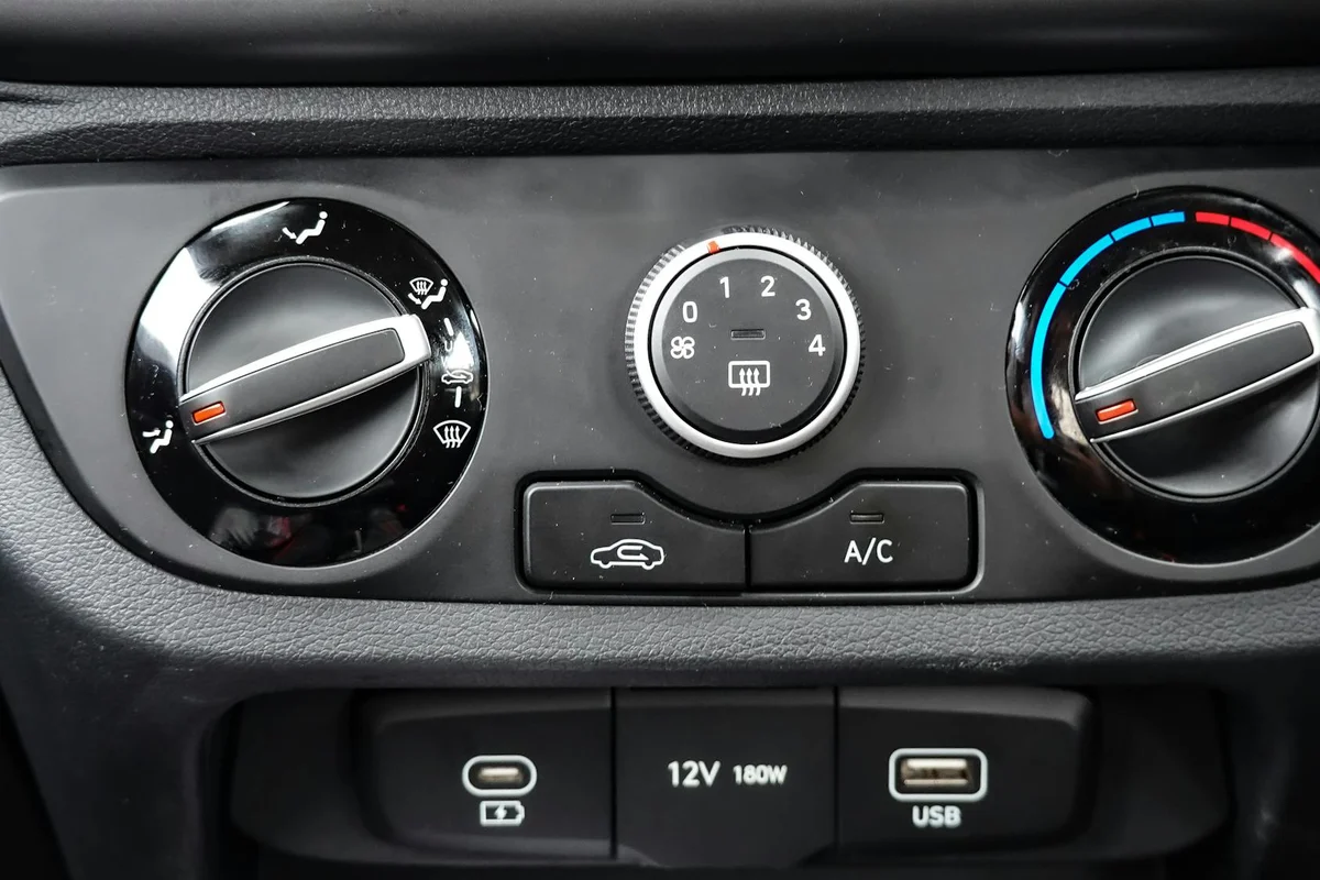 A car's dashboard shows three black rotary knobs, two buttons, and three ports, including a USB.