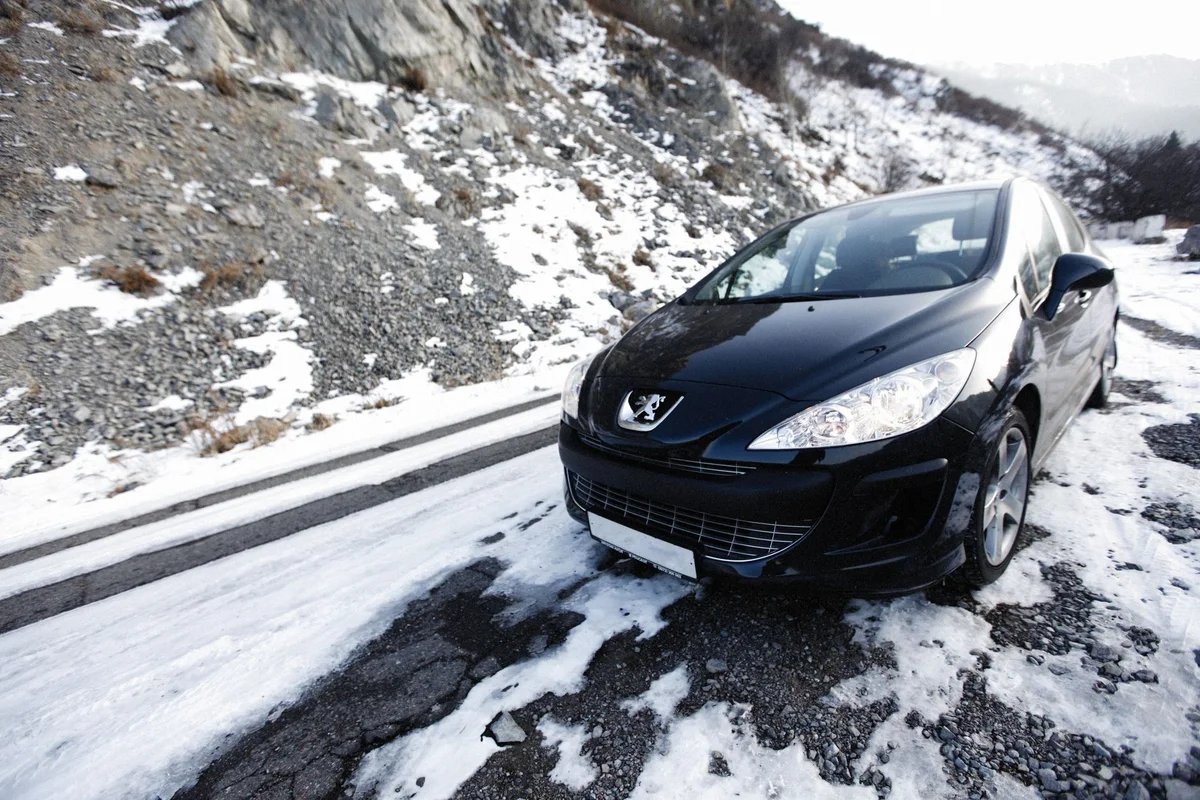 A black car navigates a snowy mountain road, showcasing winter travel and adventure.