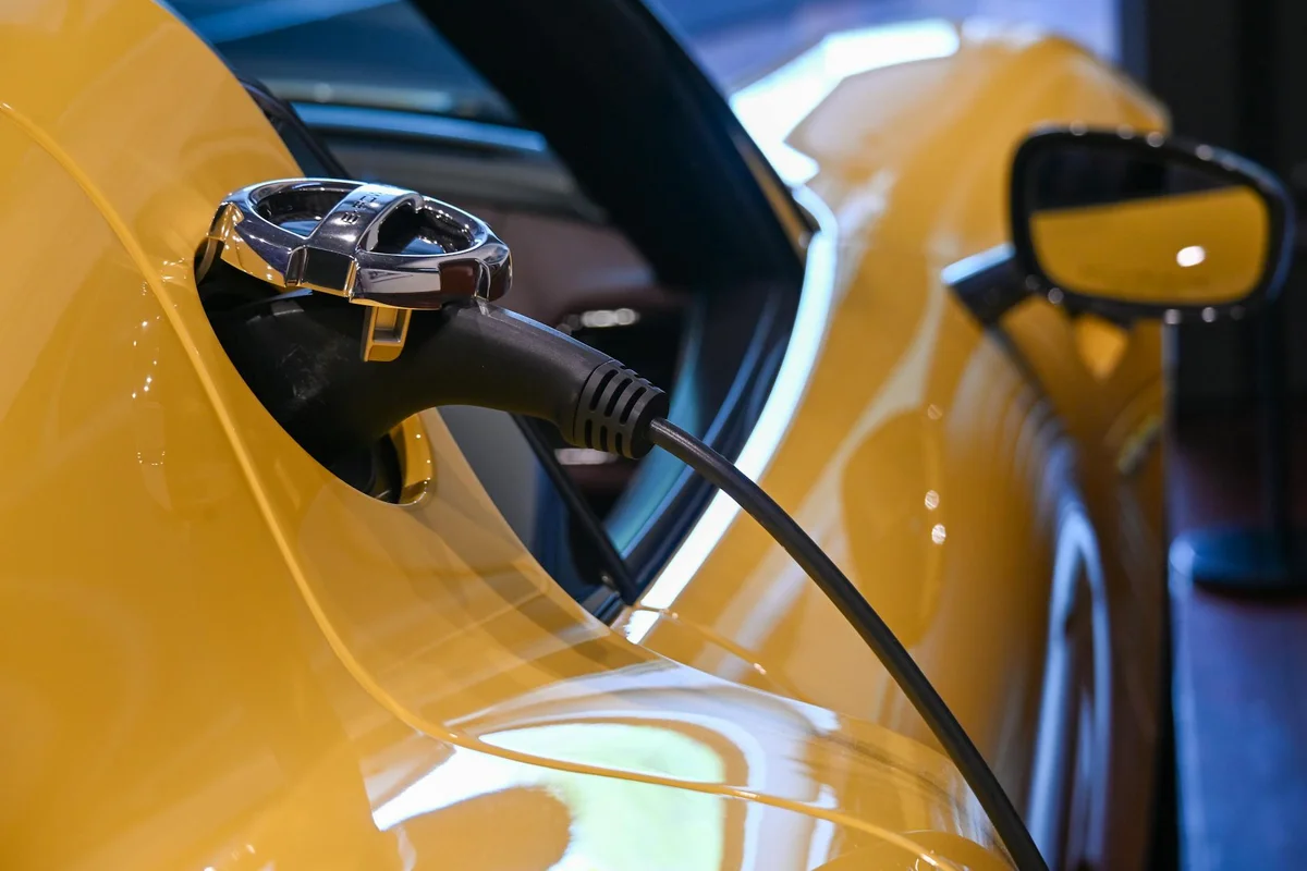 A black charging cable plugged into the side of a shiny yellow car.