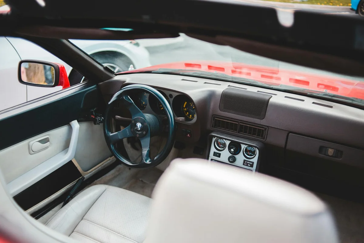 The interior of a red convertible car shows a black steering wheel, a brown dashboard, and a white leather seat.